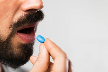 Close-up of a person holding a blue pill (viagra) near their mouth against a gray background