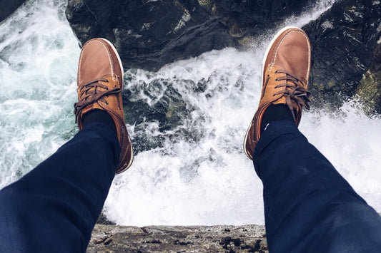 Man's feet hanging over a rock ledge above a river