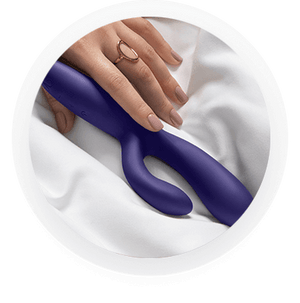 Woman's hand touching an adjustable rabbit vibrator resting on a silk sheet